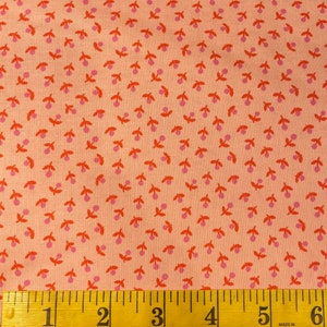 May include: A close-up of a pink fabric with a repeating pattern of small orange and pink cherries. A yellow measuring tape is at the bottom of the image.