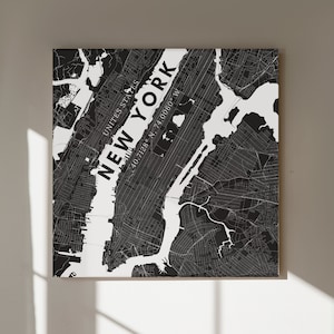 May include: Black and white map print of New York City, United States. The map shows the streets and waterways of the city. The text "NEW YORK" is written diagonally across the map, with the coordinates "40.7128° N, 74.0060° W" below it.