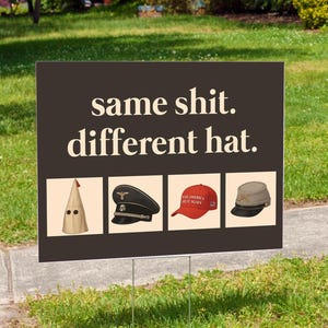 May include: A dark brown yard sign with the text "same shit. different hat." The sign features four images of different hats: a KKK hood, a black military cap, a red baseball cap, and a gray Civil War cap.