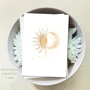 Puede incluir: Una tarjeta de felicitación rectangular blanca con una ilustración en acuarela centrada de un sol y una luna combinados en una sola forma circular. El sol tiene rayos dorados a la izquierda, mientras que la luna está a la derecha, rodeada de pequeñas estrellas.