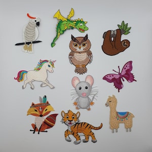 Könnte beinhalten: Eine Sammlung gestickter Aufnäher mit verschiedenen Tieren. Enthält einen Papagei, Drachen, Eule, Faultier, Einhorn, Schmetterling, Maus, Fuchs, Tiger und Lama. Jeder Aufnäher hat detaillierte Stickereien und leuchtende Farben.