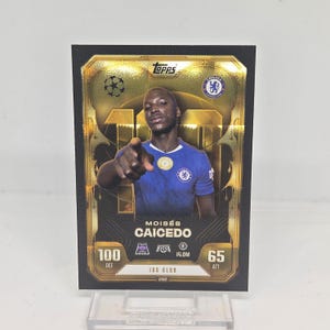 May include: A white ceramic mug with a black handle and the text "But First, Coffee" in a bold, black font. The mug is set against a blurred background, suggesting a cozy setting.