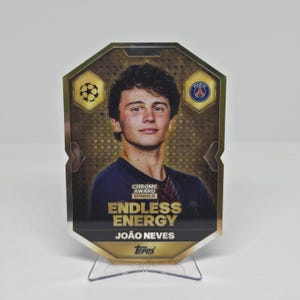 Może przedstawiać: Karta kolekcjonerska Topps Chrome Award Winner z portretem João Nevesa w ciemnoniebieskiej koszulce. Karta ma złote tło z geometrycznym wzorem, napis Endless Energy, logo Paris Saint-Germain oraz emblemat gwiazdy.