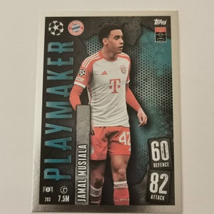 Puede incluir: Una tarjeta de intercambio plateada con Jamal Musiala, un jugador de fútbol del FC Bayern Munich. La tarjeta tiene un fondo azul y negro con un patrón hexagonal. La tarjeta tiene un borde plateado y el texto "PLAYMAKER" en letras grandes y negritas. La tarjeta también tiene el texto "60 DEFENCE" y "82 ATTACK".