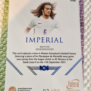 May include: A white and blue football jersey with the number 6 on the front. The jersey is worn by a player with long brown hair. The card is part of a set called "Imperial" and is numbered 03/09.