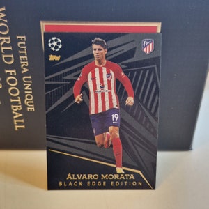 May include: A black and gold soccer trading card featuring a photo of Alvaro Morata, a soccer player wearing a red and white striped jersey with the number 19. The card is from the Futera Unique World Football Black Edge Edition series.