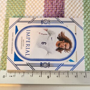 May include: A white and blue sports card featuring a photo of a football player wearing a white jersey with a blue number 6. The card has the text "IMPERIAL" and "MATTEO GUENDOUZI" on it. The card also has the text "GAME USED MEMORABILIA" on it.
