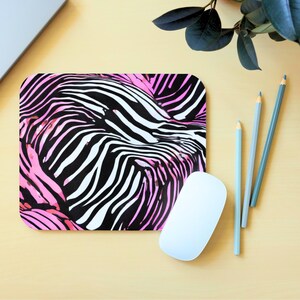 May include: A black and white zebra patterned mouse pad with pink accents. The mouse pad is on a light brown surface.