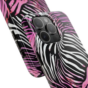 K&ouml;nnte beinhalten: Nahaufnahme von zwei Handyh&uuml;llen mit Zebrastreifenmuster. Die H&uuml;llen haben einen schwarzen Hintergrund mit wei&szlig;en und rosa Streifen. Die Handyh&uuml;lle auf der rechten Seite hat ein sichtbares Kameraobjektiv.
