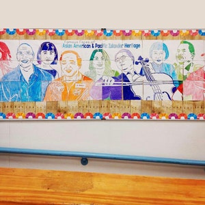 Könnte beinhalten: Ein farbenfrohes Wandbild an einer weißen Wand mit dem Titel "Famous Faces of Asian American & Pacific Islander Heritage". Das Wandbild besteht aus einzelnen Quadraten mit Porträts verschiedener Personen. Die Quadrate sind in einer Reihe angeordnet und von einem bunten Rand umgeben.