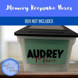 May include: A clear plastic storage box with a black lid. The box has a green label with the name "Audrey Marie" written in black and red lettering. The text "BOX NOT INCLUDED" is written in white letters on a blue background above the box.