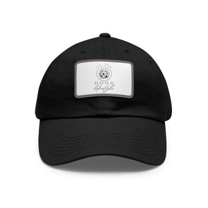 May include: Black baseball cap with a curved peak. A rectangular patch on the front features a dog illustration, the text "EST. 2021", and the words "DOOD Lifestyle" in a script font. The cap is made of a durable fabric.