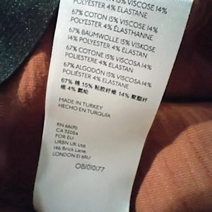 May include: A white clothing tag with text in multiple languages, including English, French, German, Spanish, Italian, and Chinese. The tag lists fabric composition percentages: cotton, viscose, polyester, and elastane. The tag also includes the text "MADE IN TURKEY".