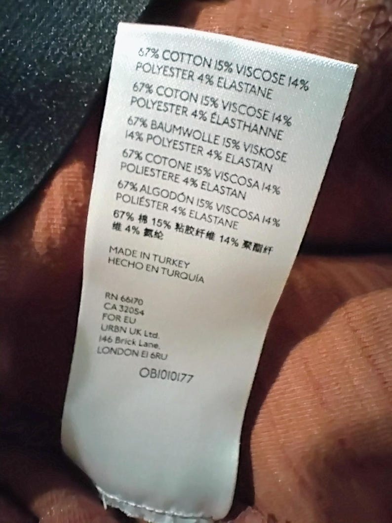 May include: A white clothing tag with text in multiple languages, including English, French, German, Spanish, Italian, and Chinese. The tag lists fabric composition percentages: cotton, viscose, polyester, and elastane. The tag also includes the text "MADE IN TURKEY".