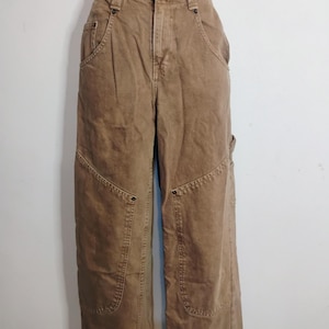 May include: High-waisted tan utility pants featuring a button closure, belt loops, and reinforced knee panels. These pants include deep front pockets with metal rivets and a side utility loop, constructed from a durable, solid-colored cotton fabric.