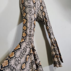 May include: A pair of flared pants with a snakeskin pattern in shades of beige, brown, and black. The pants have a high waist and a wide, flowing leg. The fabric appears to be soft and stretchy.