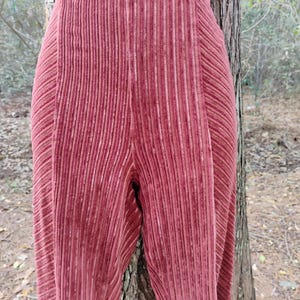 May include: Close-up of a pair of high-waisted, wide-leg pants in a deep rose color. The pants have a vertical ribbed texture, creating a subtle striped effect. The fabric appears to be soft and flowing.