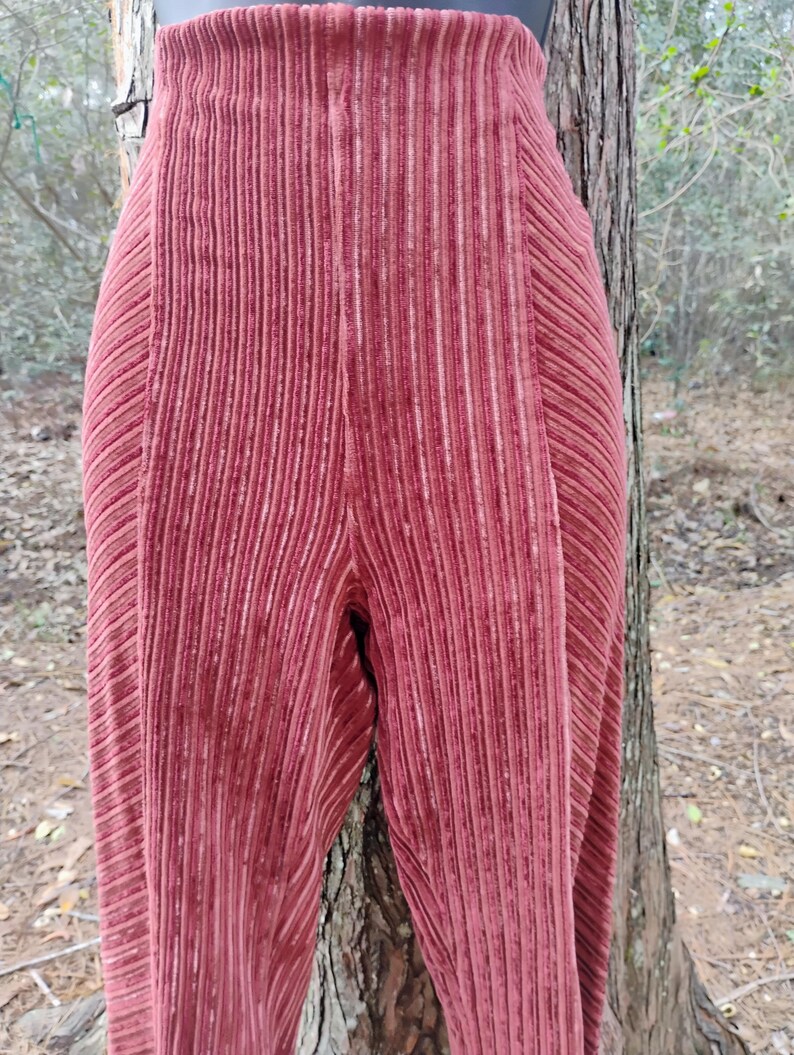 May include: Close-up of a pair of high-waisted, wide-leg pants in a deep rose color. The pants have a vertical ribbed texture, creating a subtle striped effect. The fabric appears to be soft and flowing.
