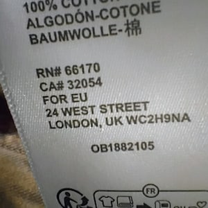 May include: A white fabric garment care label featuring black text that reads 100% COTTON- COTON ALGOD&Oacute;N-COTONE BAUMWOLLE-棉, RN# 66170, CA# 32054, FOR EU, 24 WEST STREET, LONDON, UK WC2H9NA, OB1882105, and a recycling icon with the text quefairedemesdechets.fr.