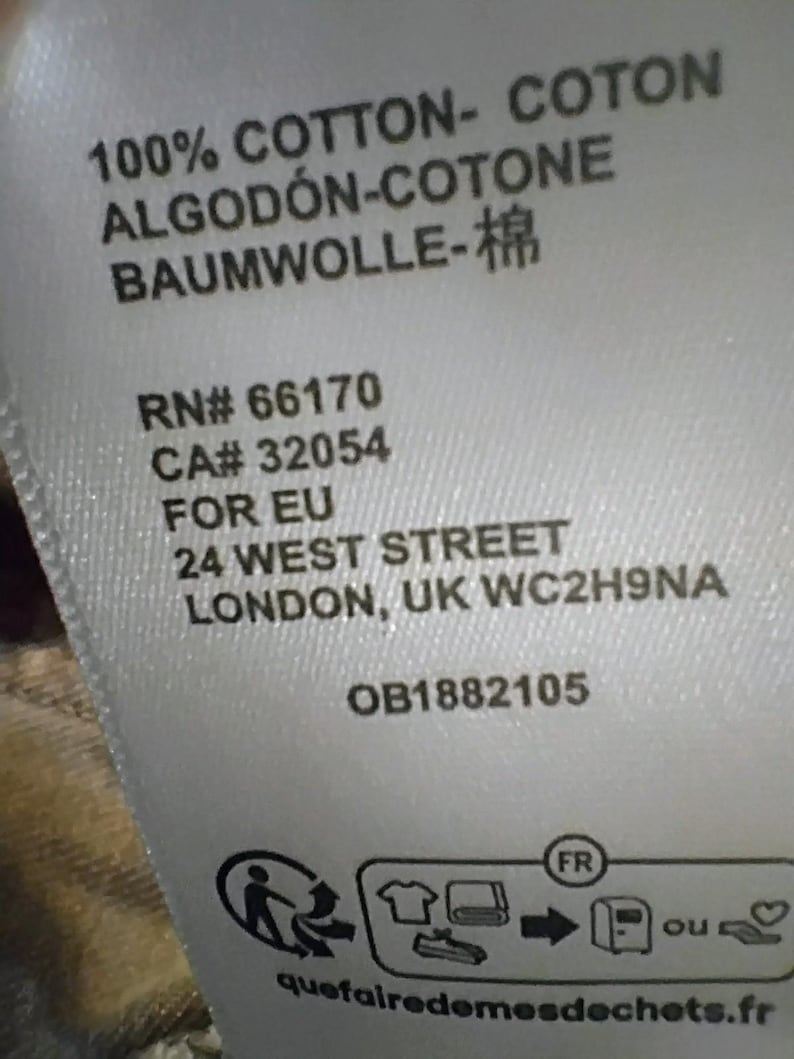 May include: A white fabric garment care label featuring black text that reads 100% COTTON- COTON ALGOD&Oacute;N-COTONE BAUMWOLLE-棉, RN# 66170, CA# 32054, FOR EU, 24 WEST STREET, LONDON, UK WC2H9NA, OB1882105, and a recycling icon with the text quefairedemesdechets.fr.