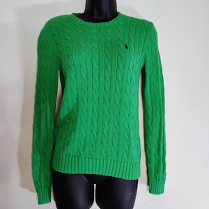 May include: Bright green cable-knit sweater with long sleeves. The sweater has a crew neck and a small black logo on the chest. The garment is displayed on a black mannequin.