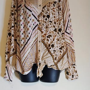 May include: A long-sleeved button-down shirt with a patchwork design. The shirt features various patterns, including stripes, floral prints, and geometric shapes in shades of beige, brown, and pink. The shirt is knotted at the waist.