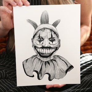 Może przedstawiać: Czarno-biały rysunek przerażającego klauna z szerokim, zębatym uśmiechem. Klaun ma spiczasty kapelusz i falbankowy kołnierzyk.