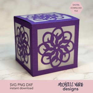 Op de afbeelding: Een paarse papieren doos met bloemvormige uitsparingen. De doos heeft een vierkante vorm met een wit interieur. Het ontwerp bevat de tekst "DIGITAL DOWNLOAD FILE" en "SVG PNG DXF instant download". De doos is een ontwerp van Michelle Ward Designs.