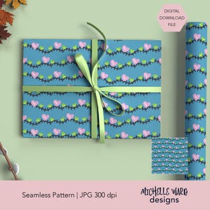 Peut inclure: Un cadeau emballé avec un fond bleu sarcelle présentant un motif répété de cœurs roses et de feuilles vertes reliés par des lignes noires. Le cadeau est noué avec un ruban vert clair. Un rouleau de papier d'emballage assorti est également visible.