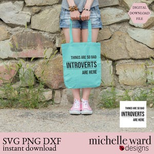 May include: A light blue tote bag with the text "THINGS ARE SO BAD INTROVERTS ARE HERE" in black. The bag is held by a person wearing denim shorts and pink sneakers. The background is a stone wall.