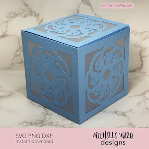 Könnte beinhalten: Eine hellblaue, würfelförmige Papierbox mit aufwendigen Ausschnitten auf jeder Seite. Die Box hat ein dekoratives Blumenmuster und ist mit "Sofort-Download" beschriftet. Design von Michelle Ward Designs.