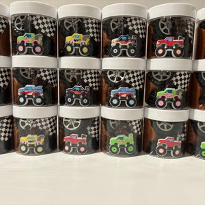 Op de afbeelding: Twaalf transparante plastic containers met zwart-wit geblokte deksels. Elke container bevat een ander gekleurd monstertruck speelgoed. De monstertrucks zijn rood, blauw, groen, geel, orange en paars.
