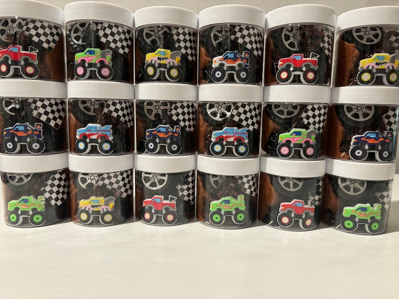 Op de afbeelding: Twaalf transparante plastic containers met zwart-wit geblokte deksels. Elke container bevat een ander gekleurd monstertruck speelgoed. De monstertrucks zijn rood, blauw, groen, geel, orange en paars.