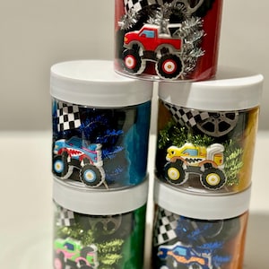 Op de afbeelding: Vier doorzichtige potten gevuld met kleurrijk klei, monstertruck speelgoed en andere kleine speelgoedjes. De potten hebben witte deksels.
