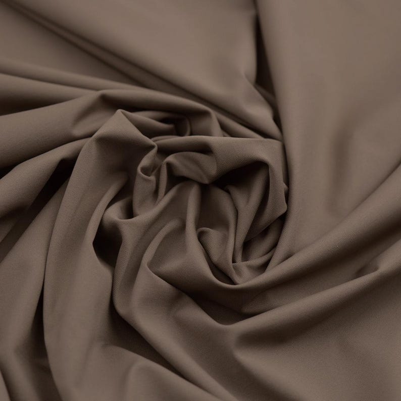 May include: Close-up of a fabric with a smooth, matte finish. The fabric is a solid, muted brown color, with soft folds and subtle shadows. The material appears to be a medium-weight textile, suitable for apparel or home decor.