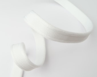 May include: A close-up of a white, curved elastic band. The band has a textured, ribbed surface on the top edge and a smooth, flat surface on the bottom. The band is against a white background.