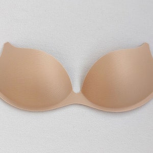 May include: A beige, strapless bra with a deep plunge neckline. The bra is made of a smooth material and has a seamless design. The cups are molded and provide support. The bra is designed to be worn under clothing.