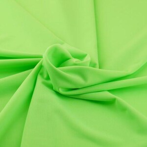 Op de afbeelding: Een close-up van een heldere, neon groene stof. Het materiaal is zacht en vloeiend, met zachte plooien en een lichte glans. De stof is in een spiraal verzameld, waardoor een textuurrijk, dynamisch beeld ontstaat.