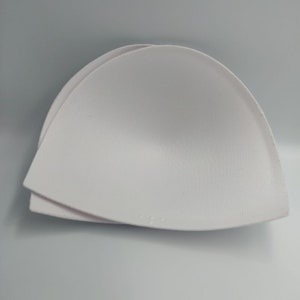 Puede incluir: Dos copas de sujetador de espuma blanca, diseñadas para agregar volumen y forma a un sujetador.