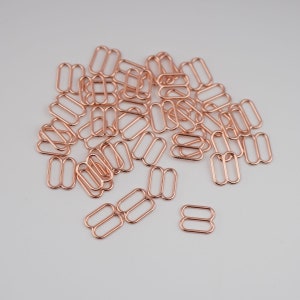 May include: A pile of rose gold metal slider buckles. The buckles are oval shaped with two holes on each side.