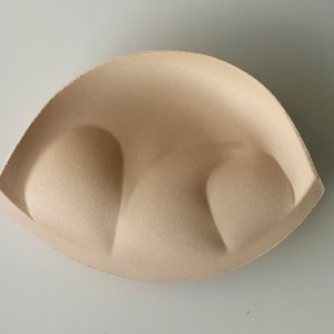 May include: A pair of beige bra cups made of foam padding. The cups are designed to provide lift and shape.