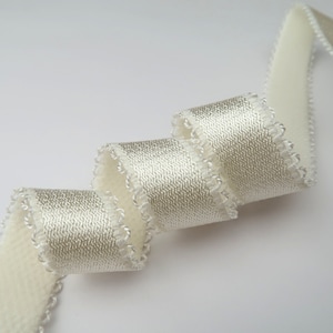 May include: A white satin ribbon with a scalloped edge. The ribbon is rolled up and has a subtle shimmer.