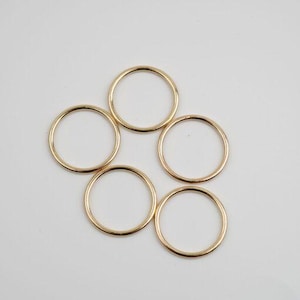 May include: Five gold-colored metal rings of different sizes. The rings are arranged in a circle, with the largest ring at the top and the smallest ring at the bottom.