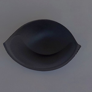 May include: A black bra cup insert made of foam. The insert is shaped like a half-circle and has a smooth surface.