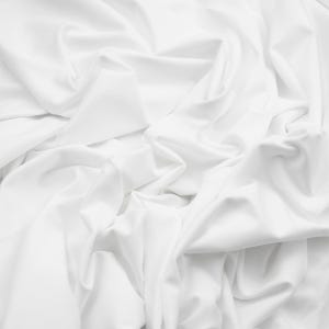 May include: A close-up shot of white fabric with soft folds and shadows. The fabric appears to be smooth and flowing, with a subtle sheen. The overall impression is one of elegance and simplicity.