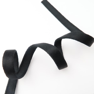 May include: Black velvet ribbon, curled and angled across a white background. The ribbon is soft and textured, with a slight sheen. The ribbon is likely used for crafts, sewing, or embellishments.