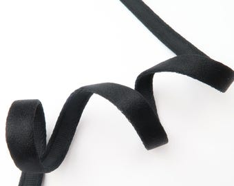 May include: Black velvet ribbon, curled and angled across a white background. The ribbon is soft and textured, with a slight sheen. The ribbon is likely used for crafts, sewing, or embellishments.