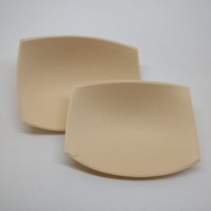 Può includere: Due inserti per reggiseno in schiuma beige. Gli inserti sono curvi e hanno una superficie liscia.