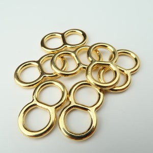 May include: A group of eight gold-colored metal rings, each with two loops. The rings are arranged in a pile, with some overlapping.