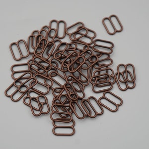May include: A pile of copper-colored metal bra strap sliders. The sliders are in the shape of a double loop.